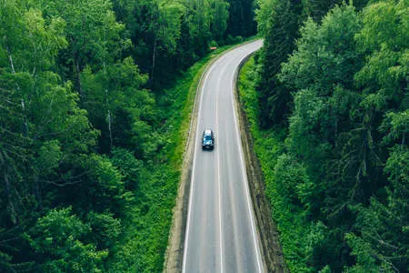 171133693-aerial-view-of-curved-country-road-with-cars-and-truck-and-green-summer-woods Aerial view of curved country road with cars and truck and green summer woods.